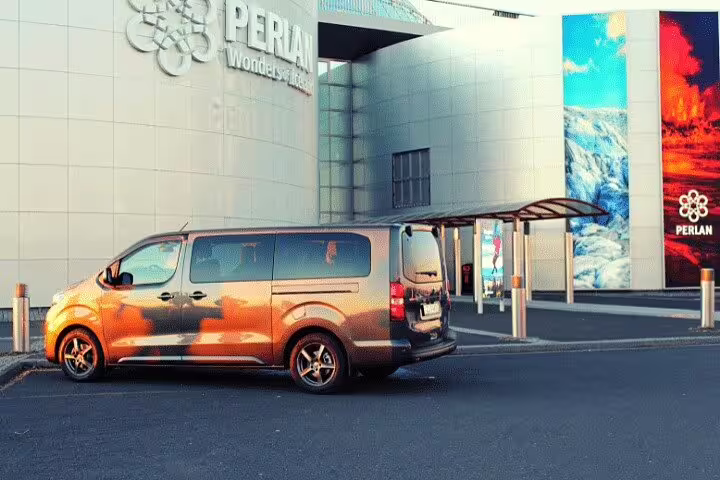 Orange private minivan parked outside Perlan building in Reykjavik for airport transfer service