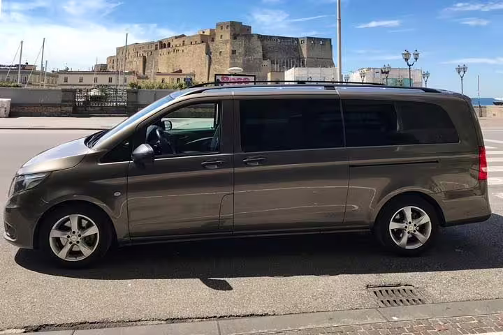 Modern private minivan for Roma to Amalfi coast transfer parked by the seafront with historic castle in the background