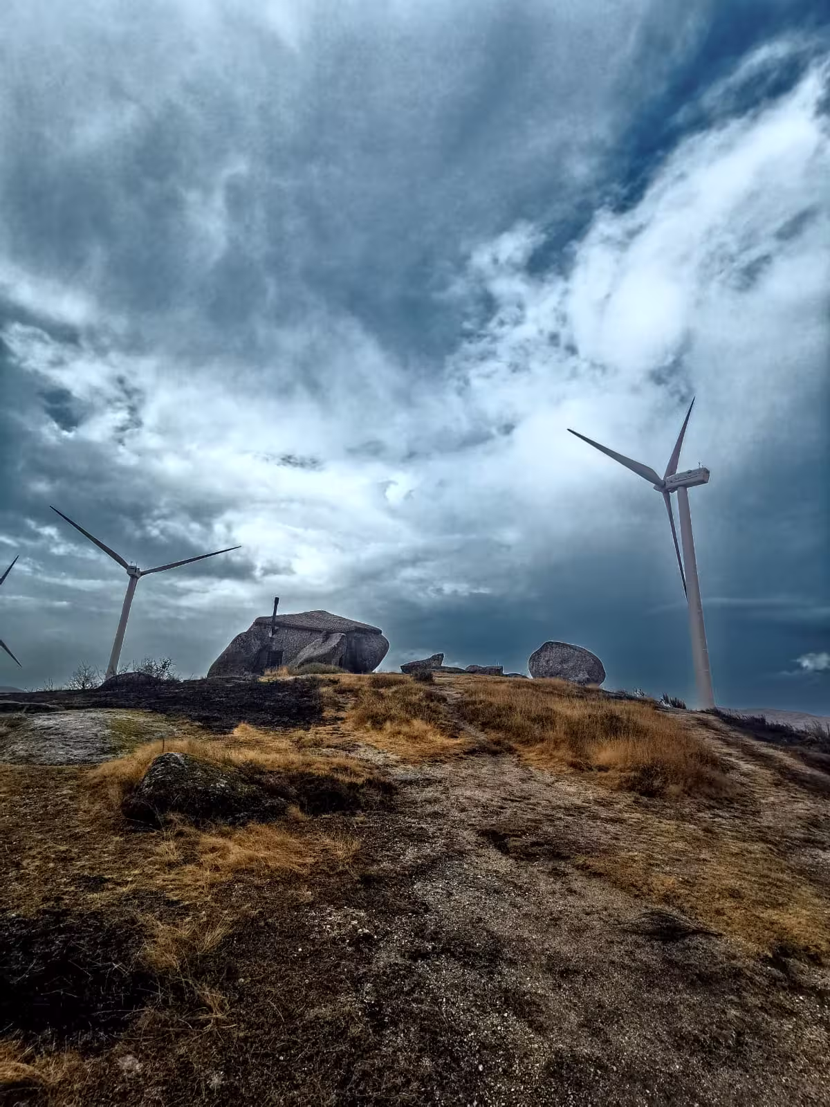 Wind turbines on rocky hillside under dramatic sky, highlighting sustainable elements of private nature tour.