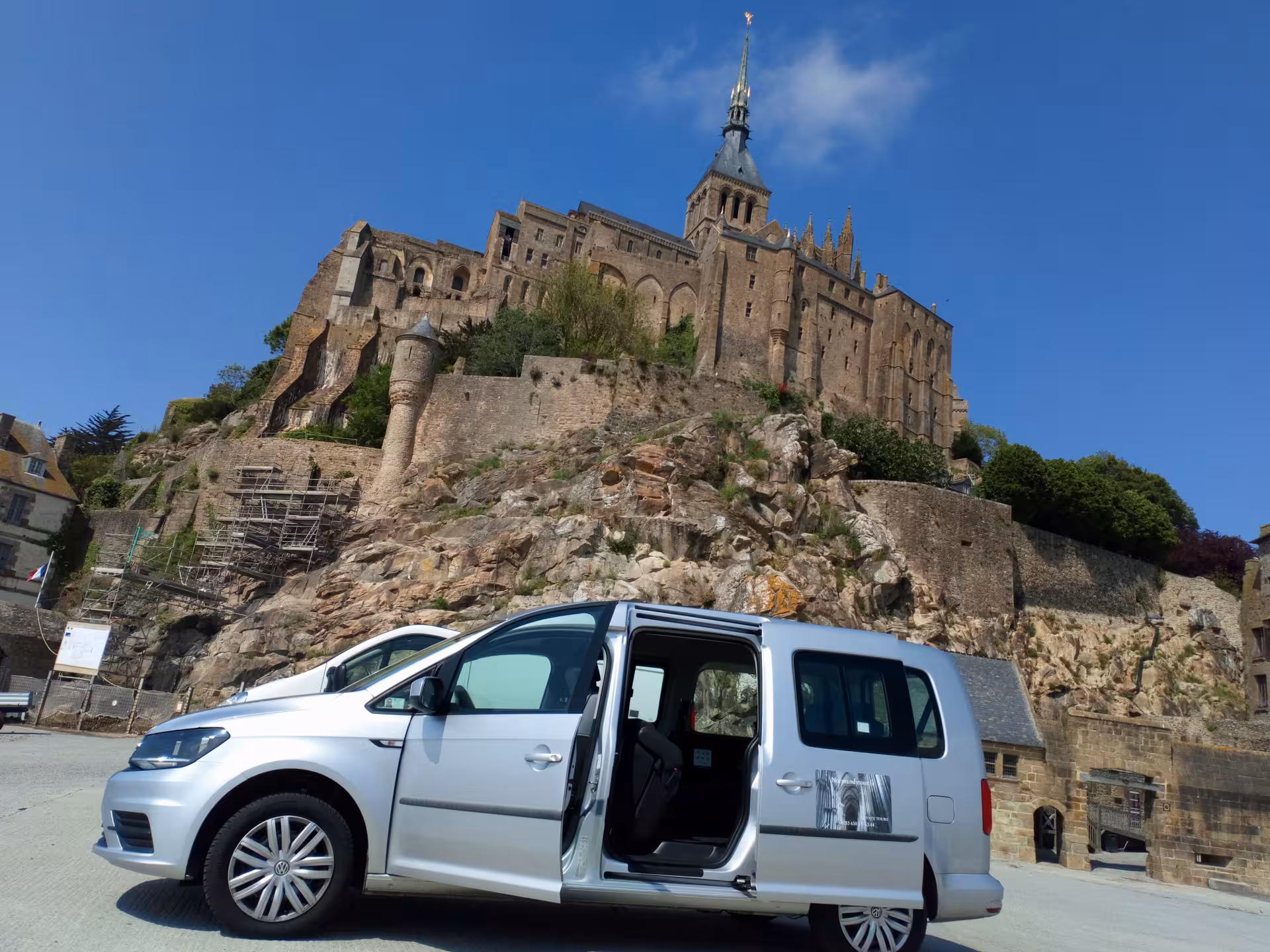 Silver Volkswagen Caddy van with open door parked in front of Mont Saint-Michel abbey, Normandy, France