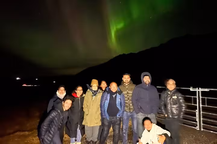 Group of tourists posing under vibrant green northern lights aurora borealis in Reykjavik Iceland at night