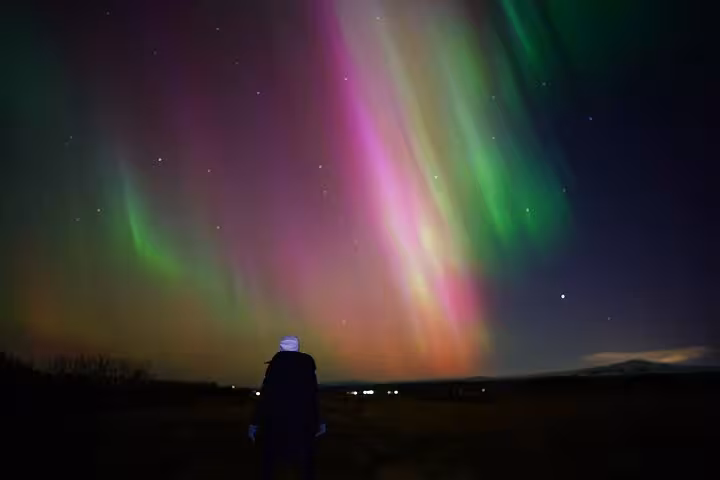 Person watching vibrant pink and green northern lights aurora borealis in Reykjavik night sky