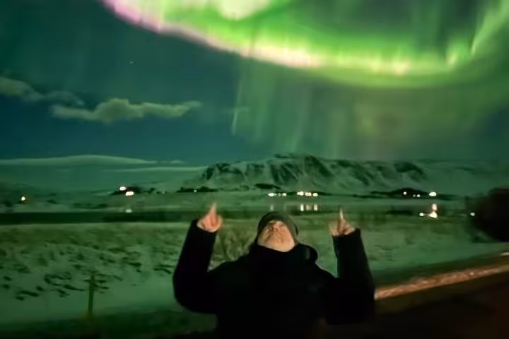 Tour guide pointing at vibrant green northern lights aurora borealis over snowy Reykjavik landscape at night