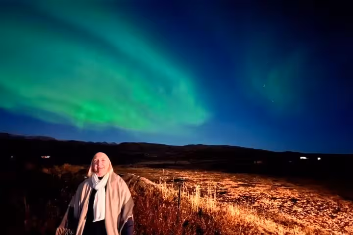 Smiling woman standing under vibrant green northern lights aurora borealis in Reykjavik Iceland at night