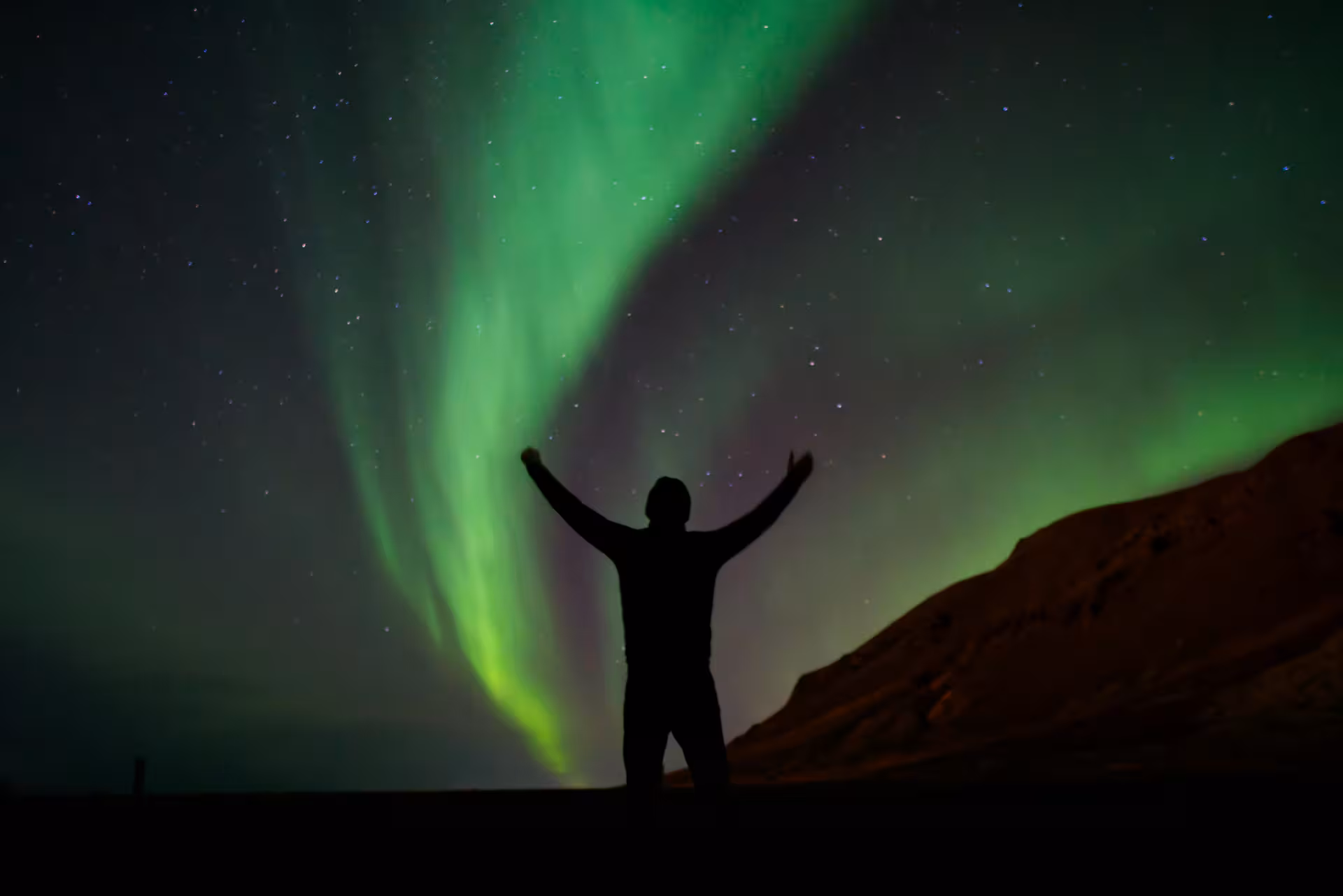 Silhouette of person with arms raised under vibrant green aurora borealis in night sky