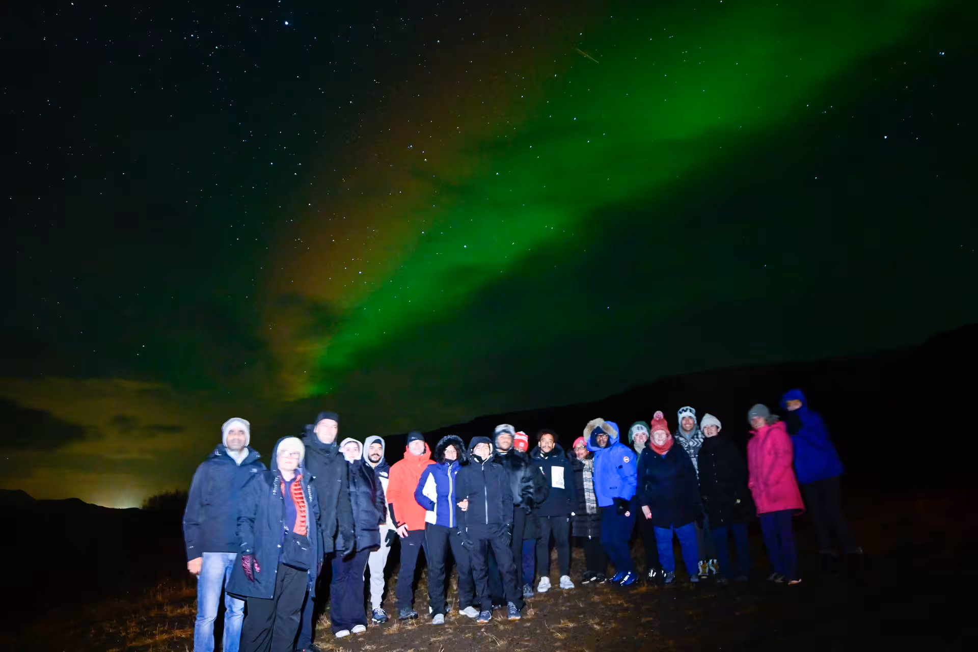 Tour group posing under brilliant green northern lights on a private guided aurora tour from Reykjavik Iceland