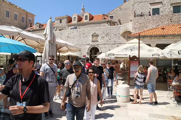 Travelers on a private Old Town walking tour through a lively square with cafes and medieval walls