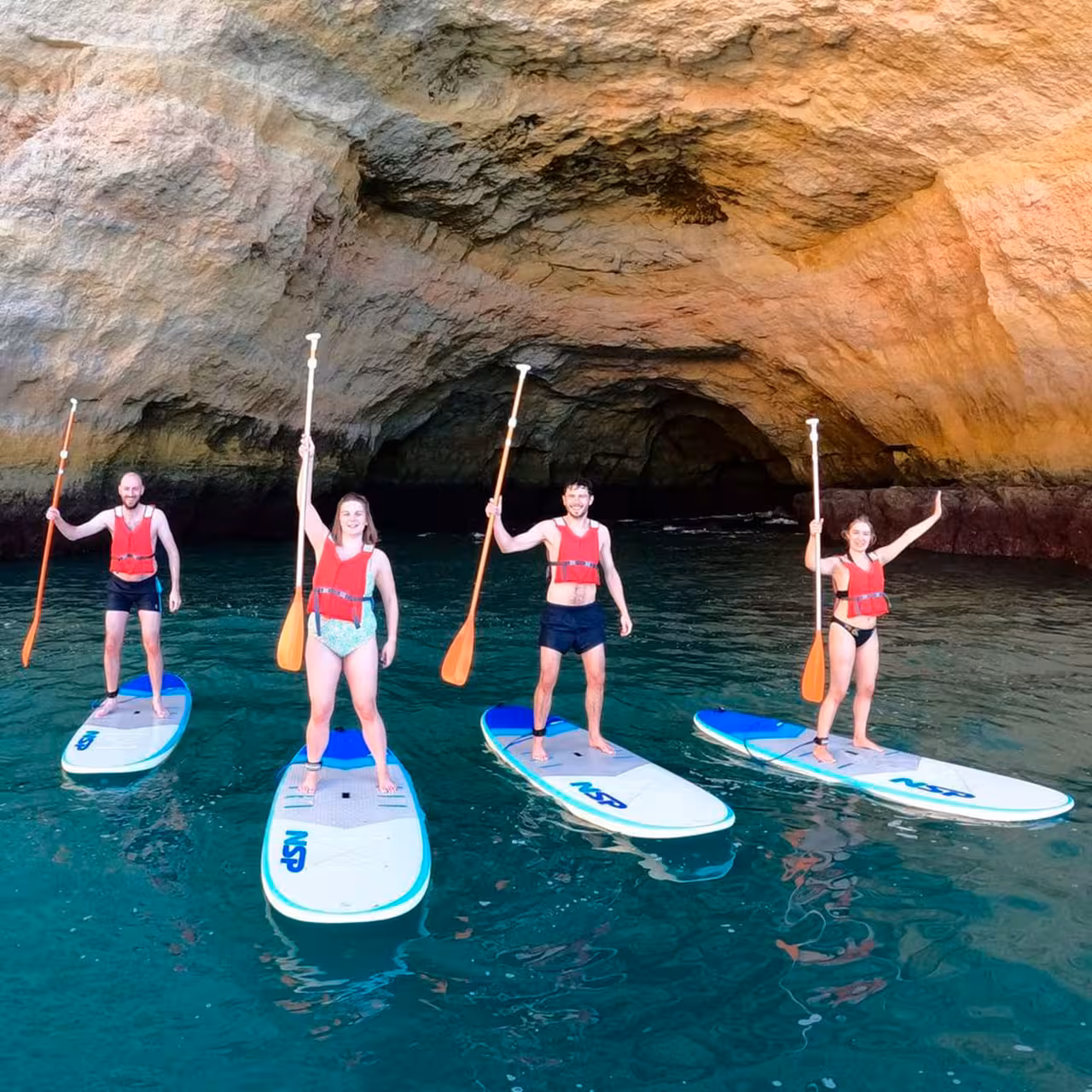 Happy group posing on paddleboards in a picturesque cave during a private paddleboarding lesson.