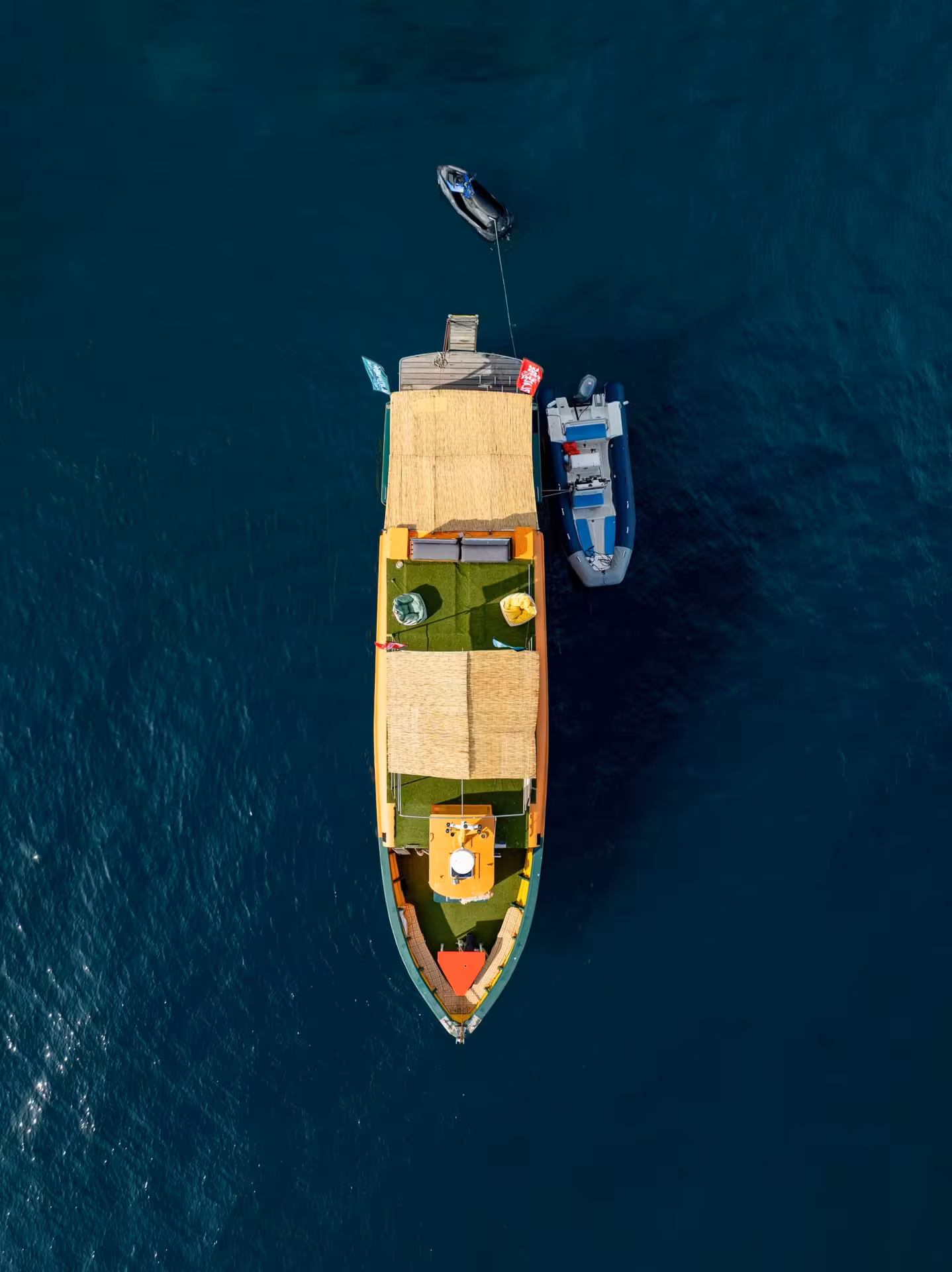 Aerial view of a decorated party boat with thatched roof and inflatable dinghy on the Cannes Riviera