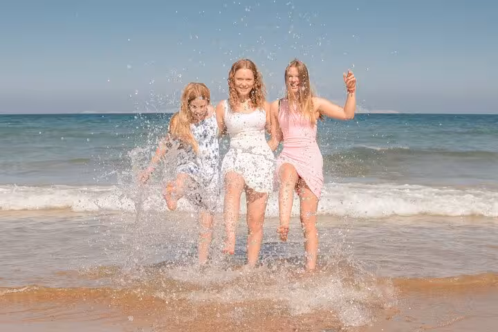 Three women joyfully splashing water at Heraklion beach, enjoying a lively private photoshoot under clear blue skies.