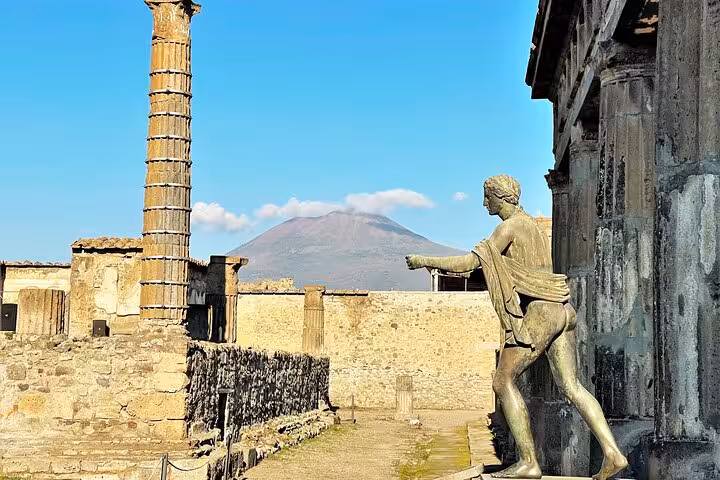 Explore ancient Pompeii ruins with a statue and Mt. Vesuvius in the background on a private skip-the-line tour.