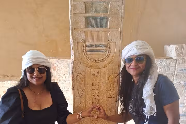 Two tourists in sunglasses and headscarves pose with ancient Egyptian hieroglyphics on the Private 3 Days Pyramids Tour.