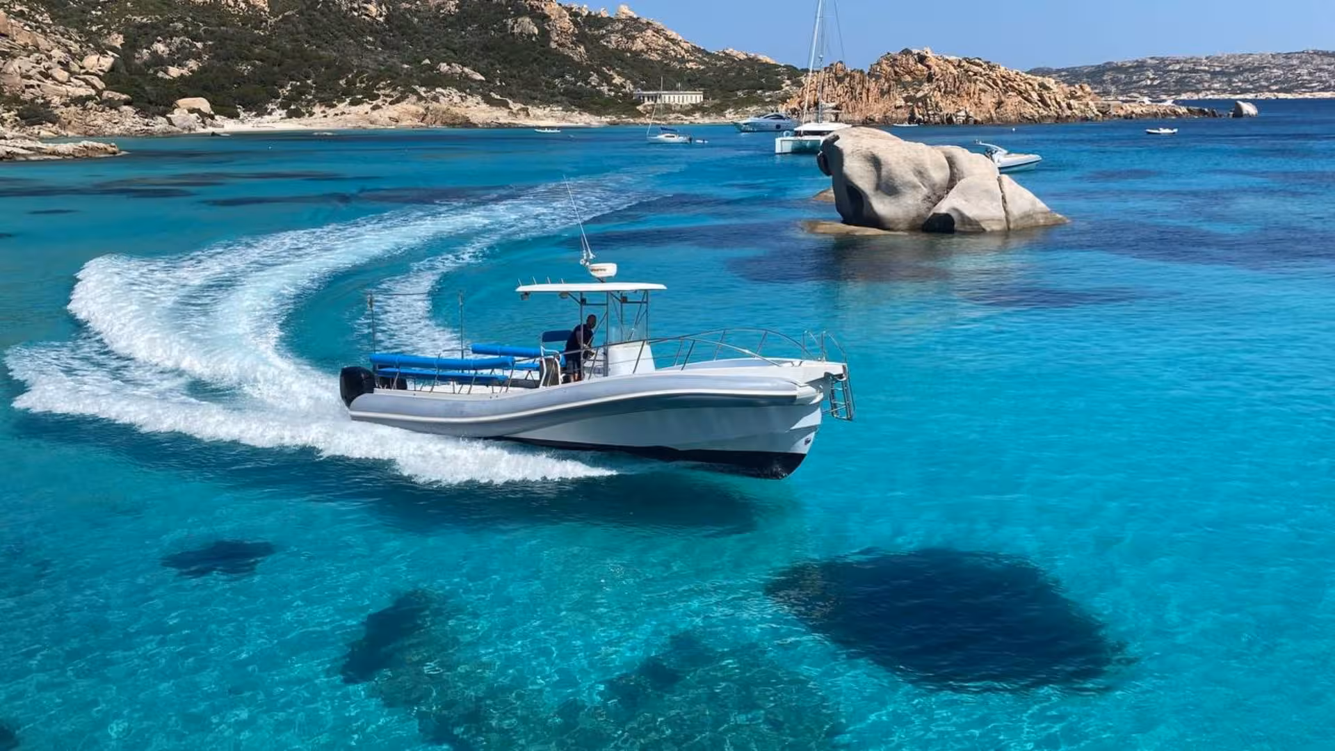 Private RIB cruising through vibrant blue waters near Santa Teresa di Gallura with scenic rocky backdrop.