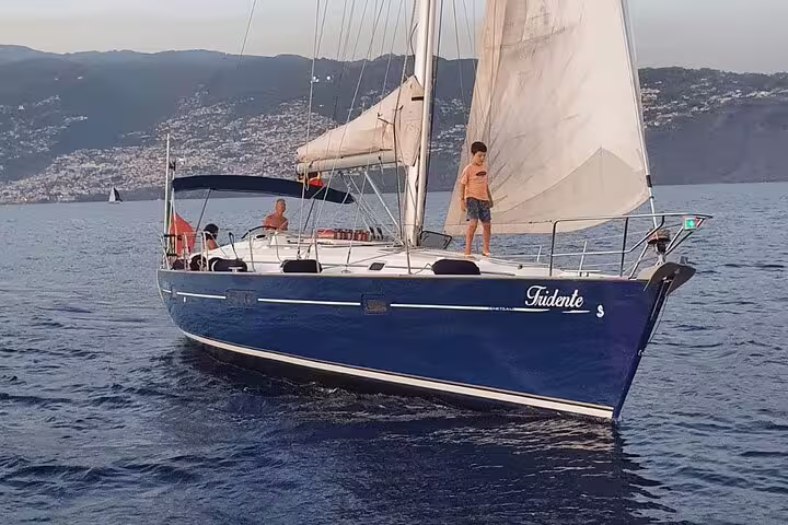 A luxurious private sailboat cruises along a scenic coastline, offering a full-day sailing adventure on tranquil blue waters.