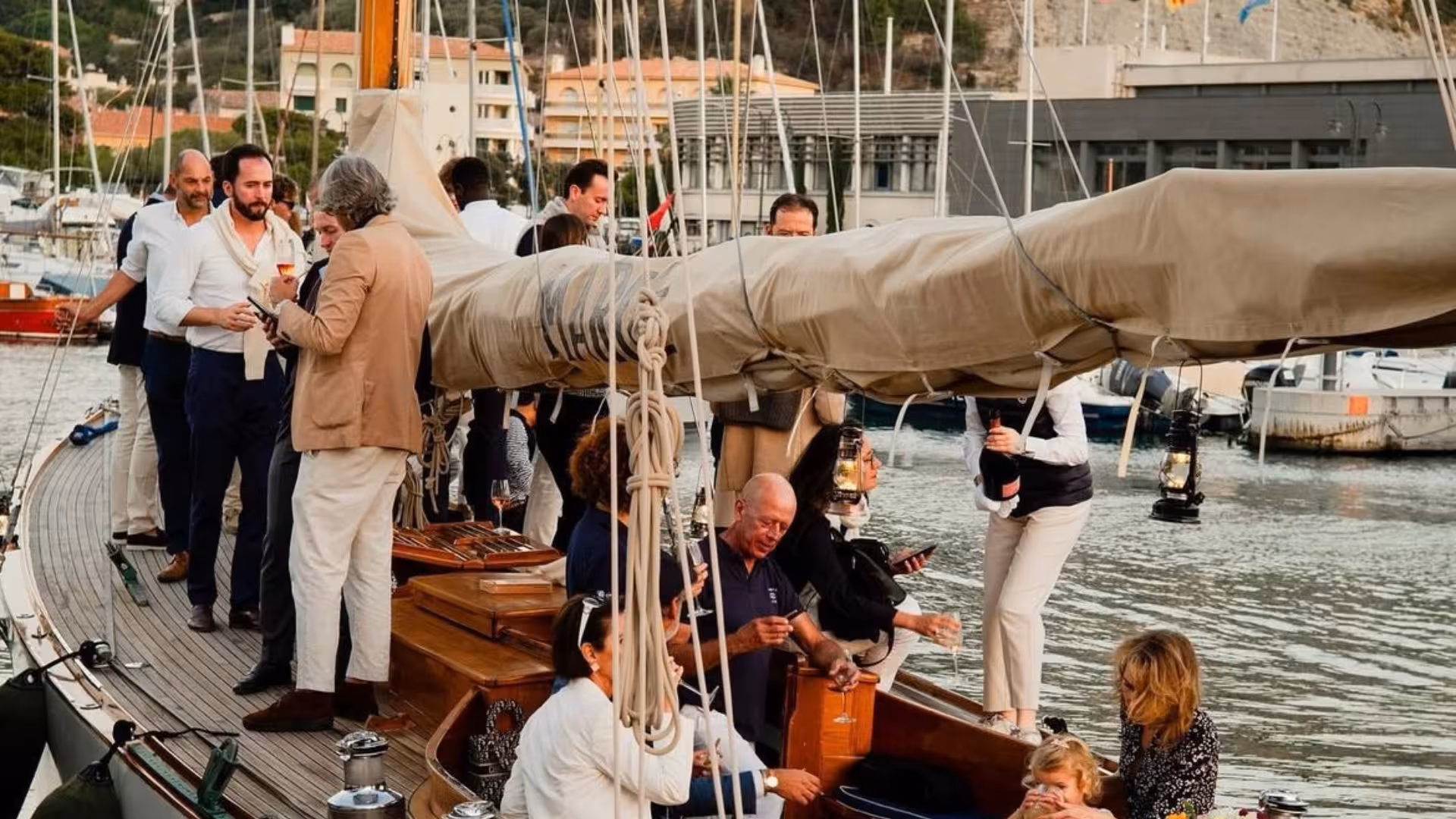 Guests enjoying drinks on a classic wooden sailing boat docked in Portofino harbor at sunset