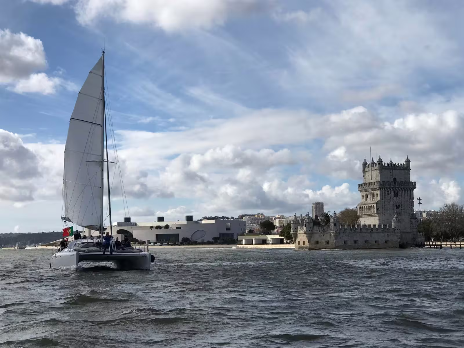 Private catamaran tour passing by the historic Belém Tower in Lisbon with sails unfurled.