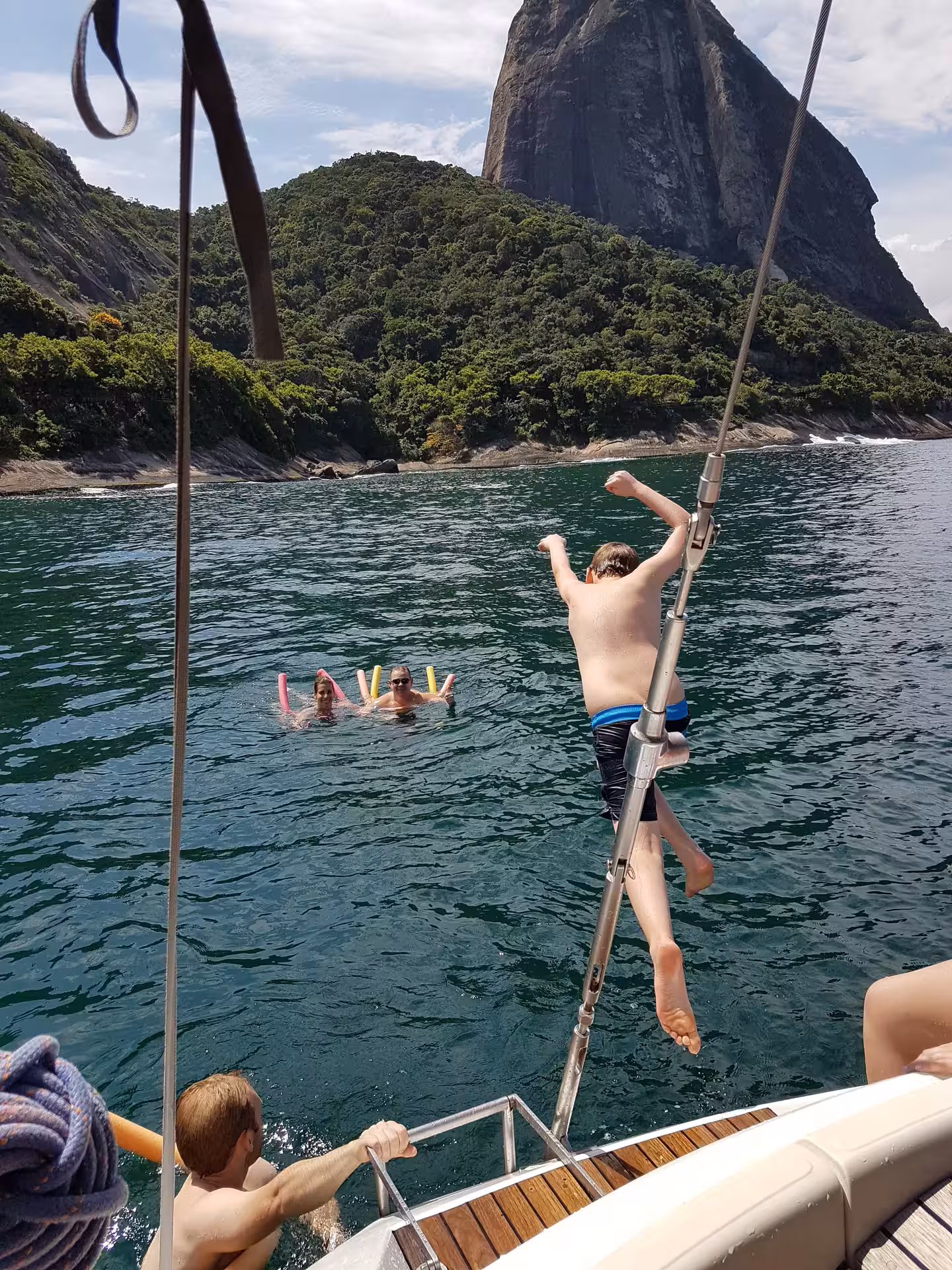 Person diving from a sailboat into crystal-clear water with scenic cliffs in the background on a private sailing tour.