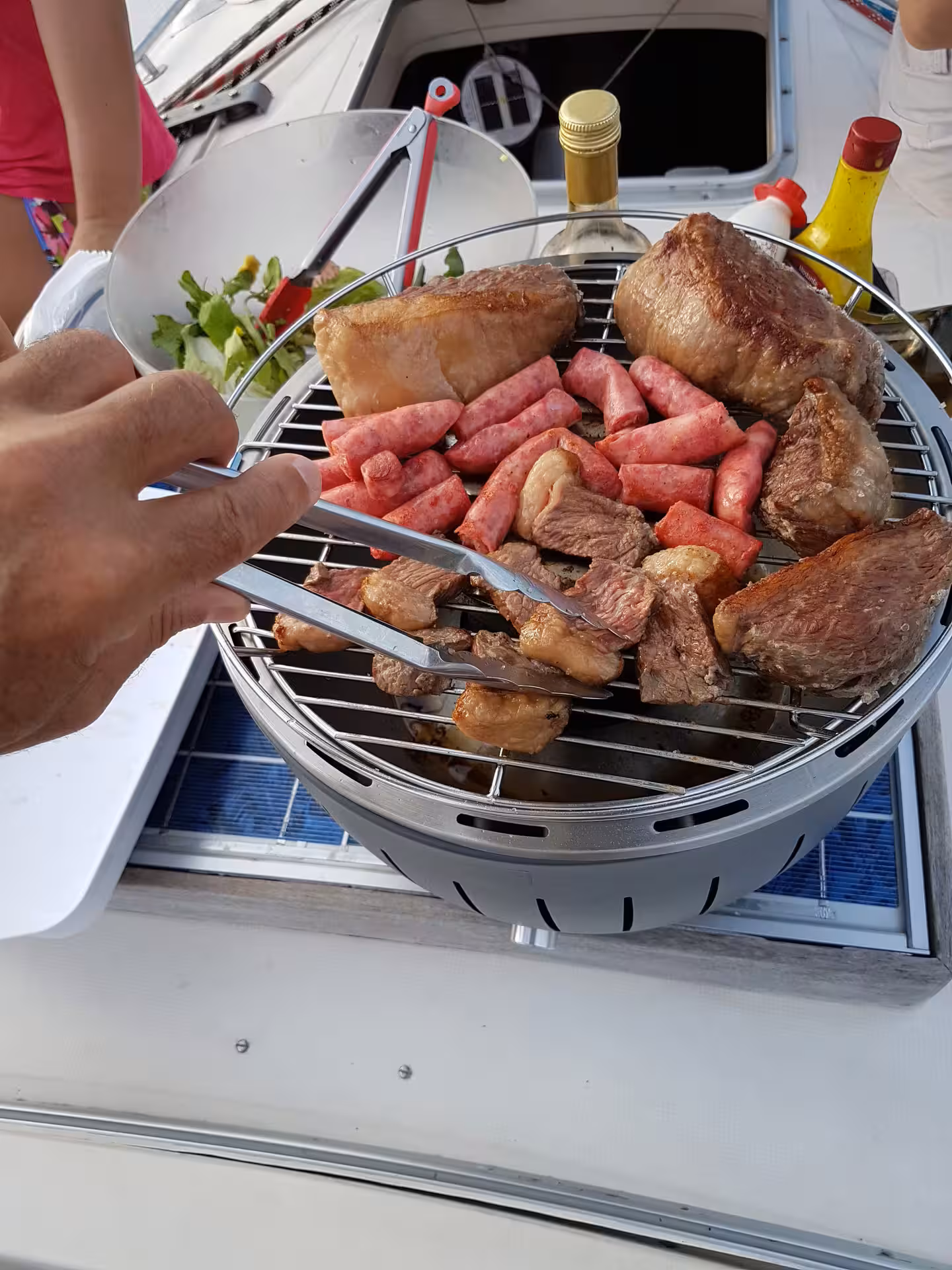 Grilling assorted meats on a portable barbecue during a private sailing tour near KAMEHAMEHA.