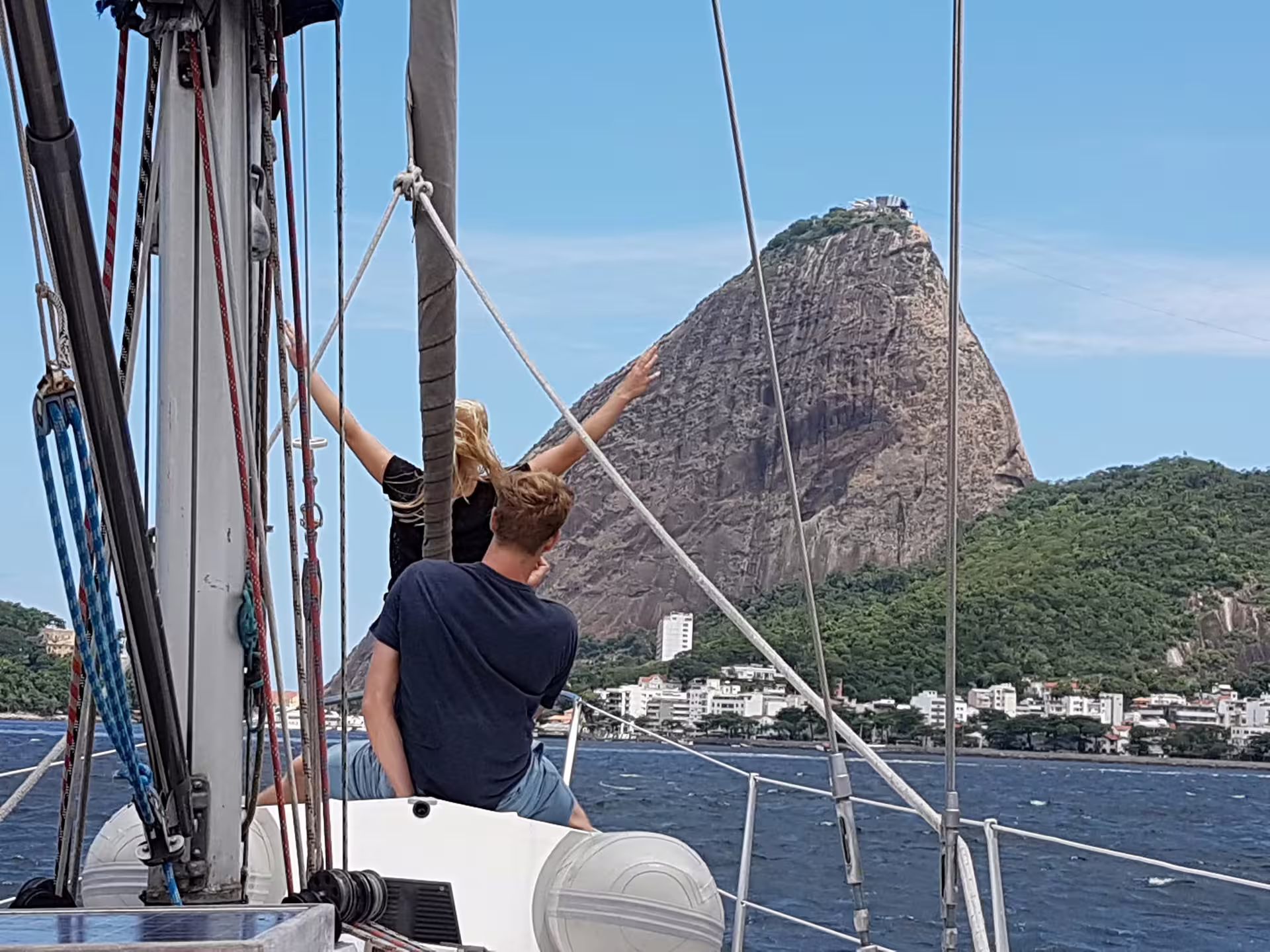 Two people on a sailboat with a view of a large rock formation on the Private Sailing Tour KAMEHAMEHA in clear weather.