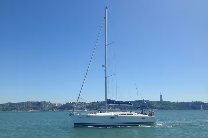 Sailboat gliding on Lisbon's serene waters with scenic views and clear blue skies during a private sailing tour.
