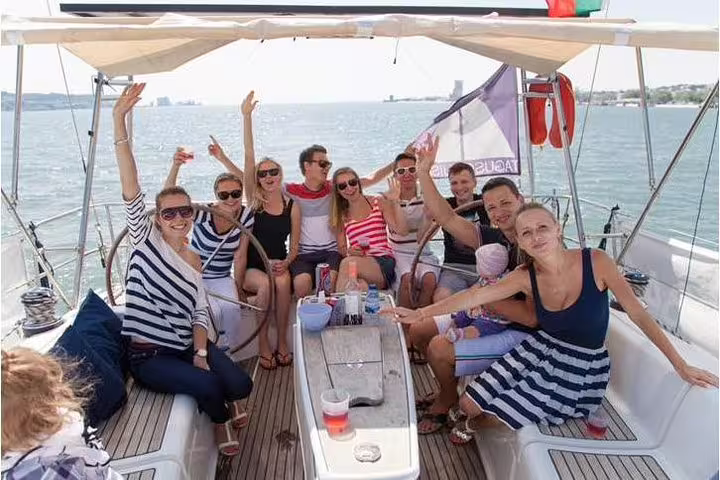 Group of friends enjoying drinks and sunshine aboard a yacht during a private sailing tour in Lisbon.