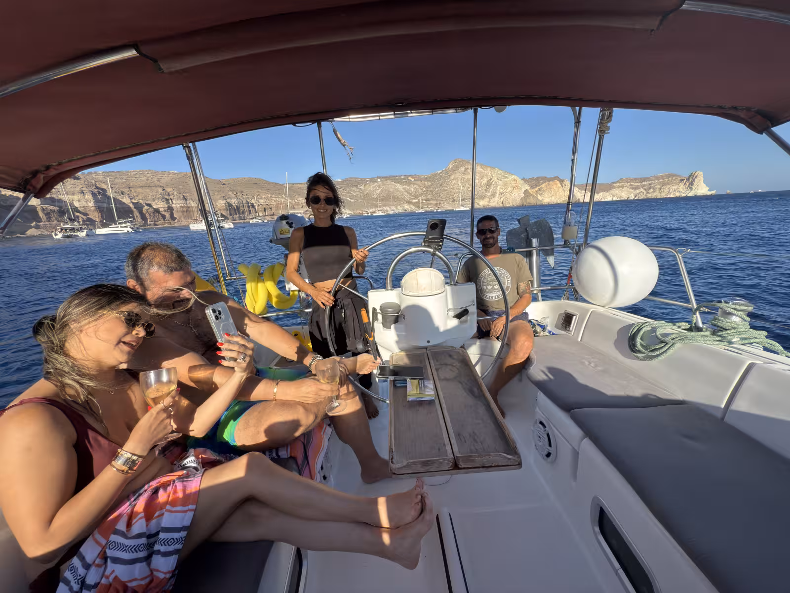 Guests relax on a private Santorini sailing day tour yacht, cruising the caldera with drinks and sea views