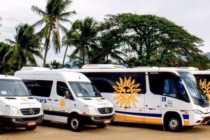 Private shuttle buses parked amidst palm trees for scenic transport from Rio de Janeiro to Buzios.