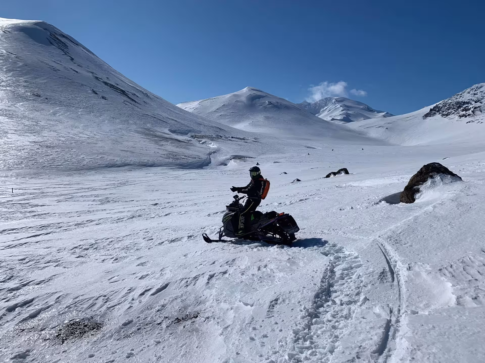 Snowmobile rider on snowy Eyjafjallajokull glacier with volcanic mountain peaks under blue sky