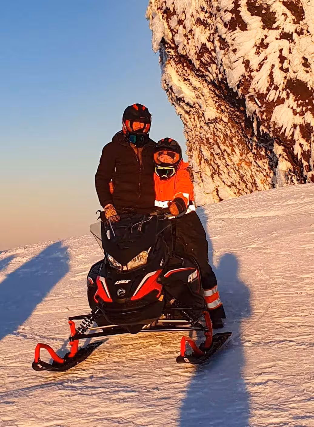 Two riders on a Lynx snowmobile on snowy Eyjafjallajokull glacier at golden hour