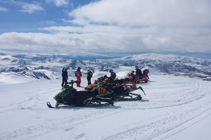 Group of snowmobilers parked on Eyjafjallajokull glacier with snowy mountain panorama in Iceland