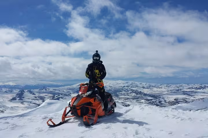 Rider on orange snowmobile atop Eyjafjallajokull glacier with panoramic snowy mountain landscape