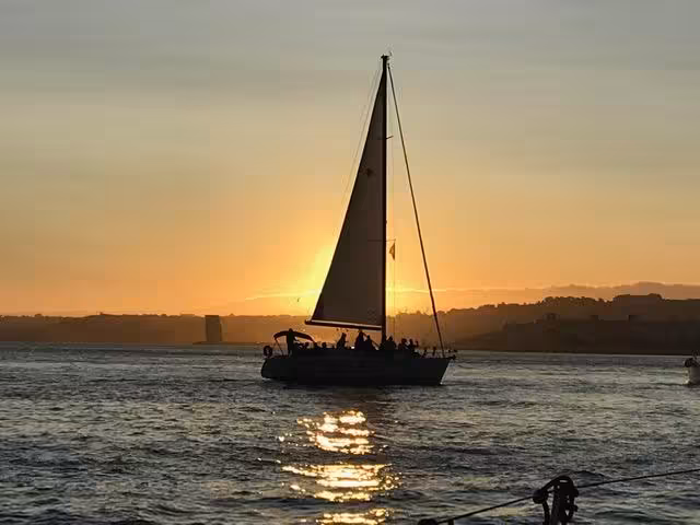 Private Sunset Lisbon Tour on Tagus River with silhouetted sailboat at dusk and Lisbon coastline in the back