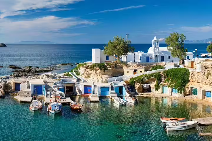 Scenic view of motorboats docked by the picturesque whitewashed village of Milos, Greece, ideal for a private sunset tour.