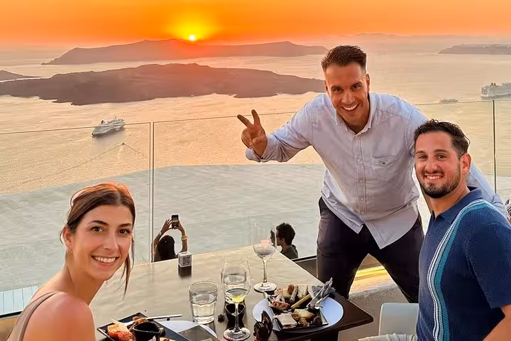 Guests enjoy tapas and wine on Santorini caldera terrace at sunset during private 3-winery wine tour