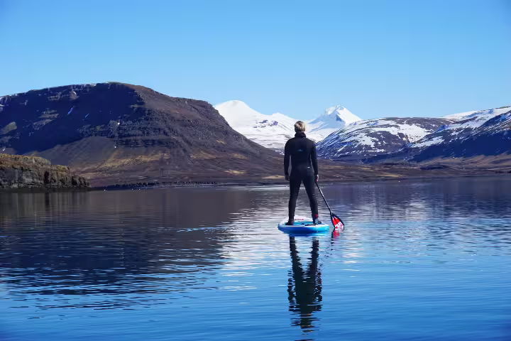 Paddle boarder explores serene waters surrounded by majestic snow-capped mountains on a private SUP tour in the forgotten fjords.