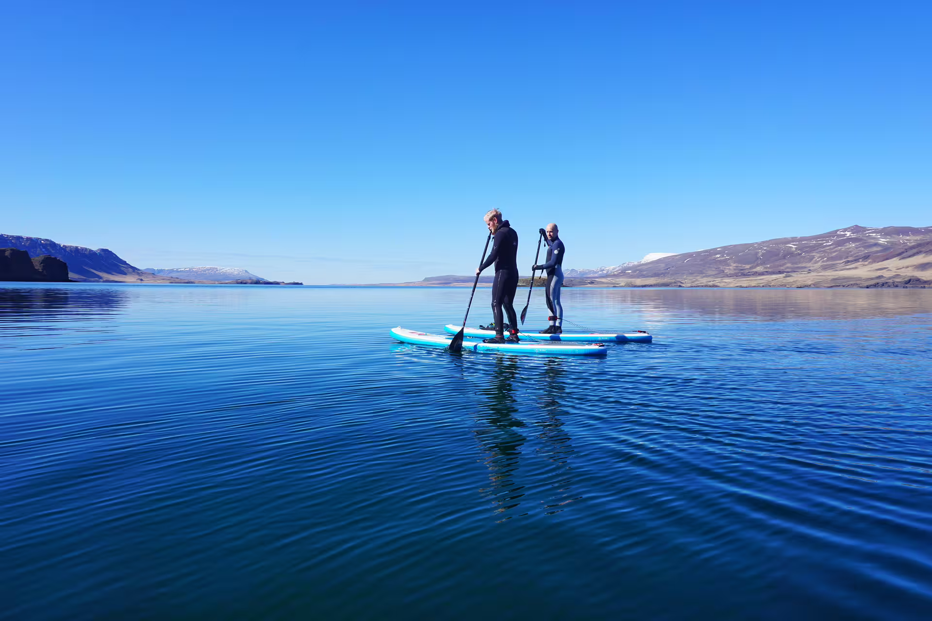 Paddle boarders explore the serene and stunning Forgotten Fjords under clear blue skies on a private SUP tour adventure.