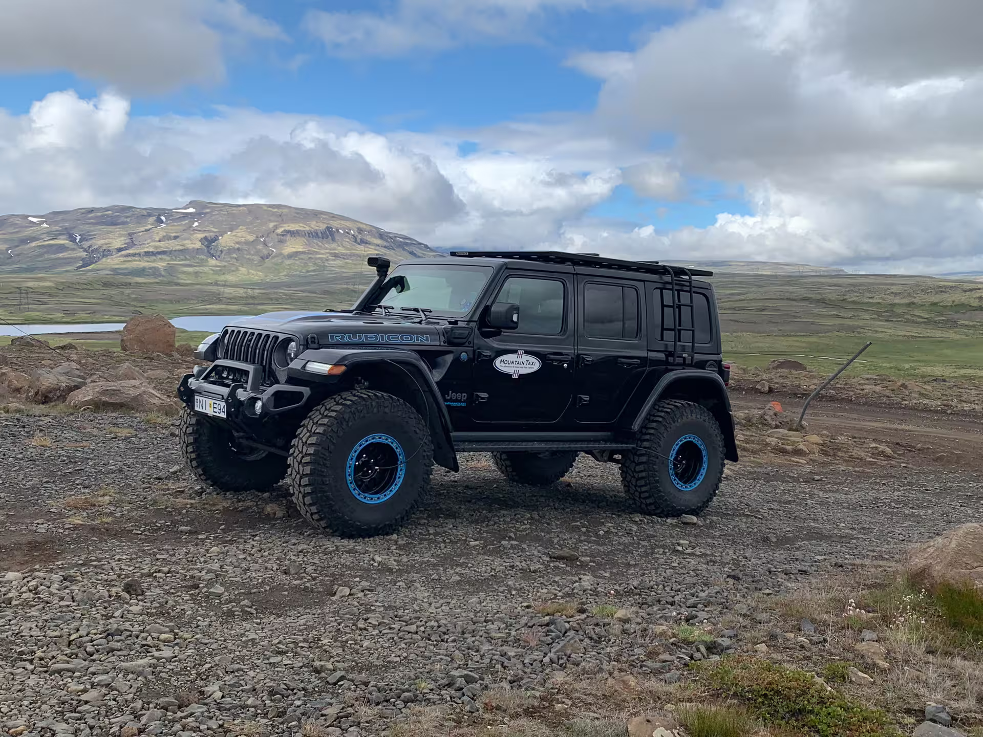 Black Jeep Wrangler Rubicon super jeep on rocky terrain with Icelandic mountains and sky backdrop