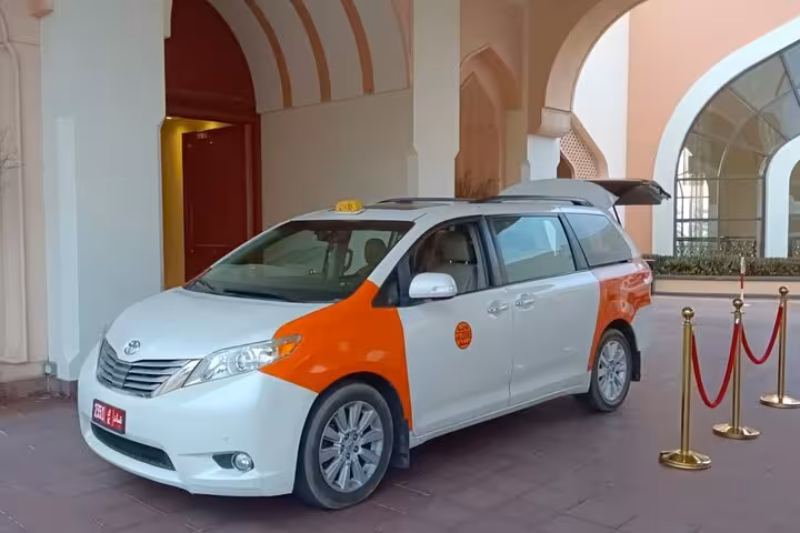Comfortable private taxi minivan outside Muscat hotel, ready for door-to-door transfer service to Nizwa, Oman