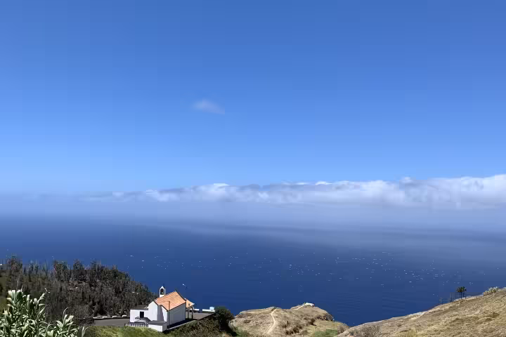 Scenic coastal view featuring lush green hills, a solitary house, and the vast blue ocean under a clear sky for private tours.