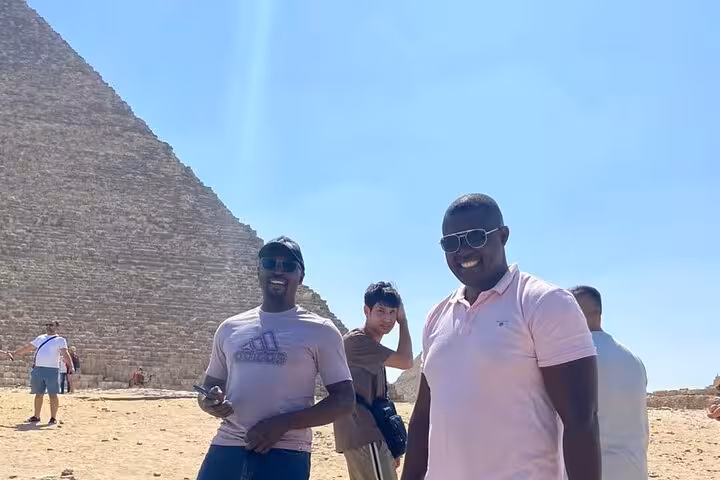Travelers posing by the Great Pyramid of Giza on a private tour with Sphinx visit, camel ride and quad bike