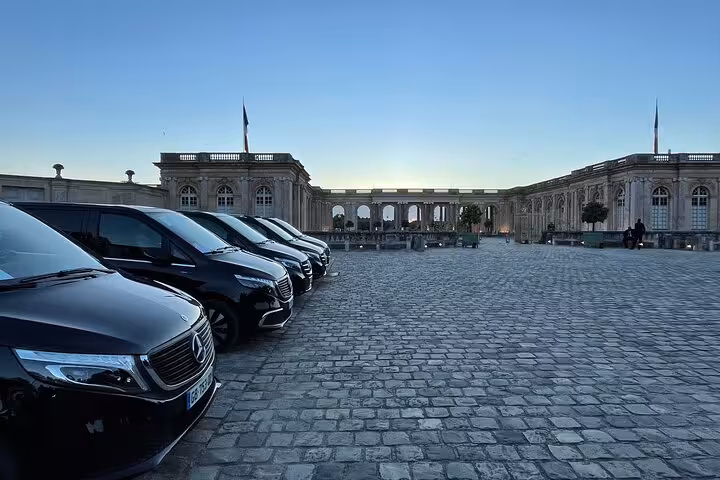 Fleet of black Mercedes vans parked on cobblestones outside the Palace of Versailles at dusk