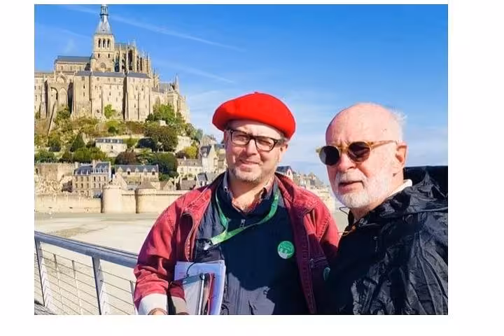 Two men posing in front of Mont-Saint-Michel abbey on a sunny day