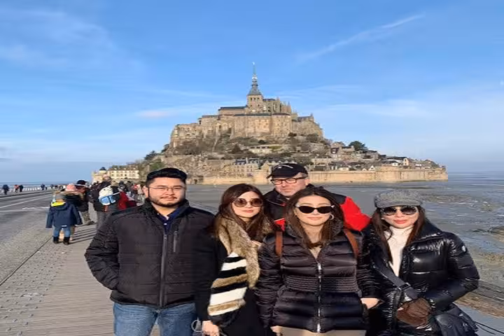 Group of tourists posing in front of Mont Saint-Michel island abbey on a clear day