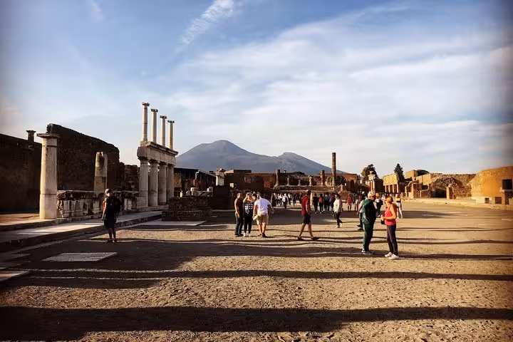Visitors exploring the ancient ruins of Pompeii with Mount Vesuvius in the background.
