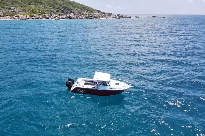 Boat cruising in the vibrant turquoise waters of La Digue, ideal for exploring during a private full-day island tour.