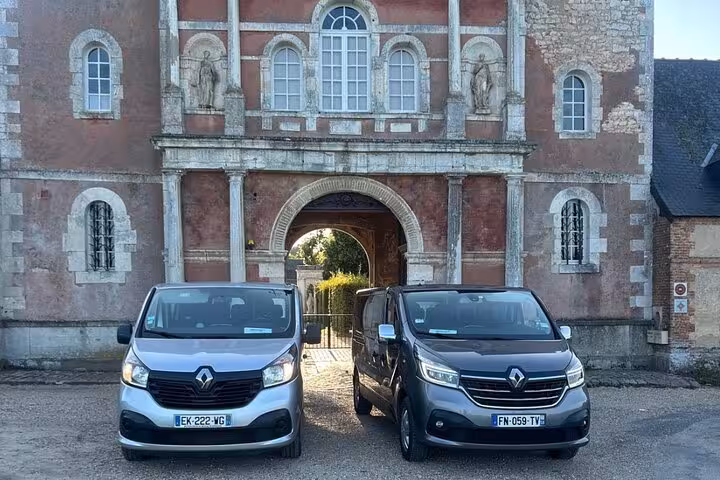 Two Renault Trafic vans parked in front of a historic French château gateway in Normandy