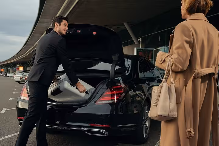Chauffeur loading luggage into black luxury sedan trunk for private transfer service at airport