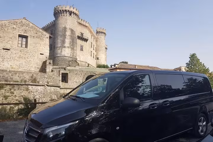 Black van parked in front of a historic castle, showcasing private transfer from Civitavecchia to Rome.