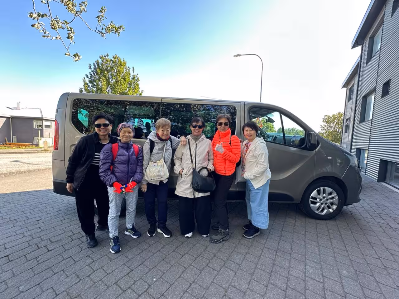Group of six travelers posing in front of a private van for airport transfer in Iceland