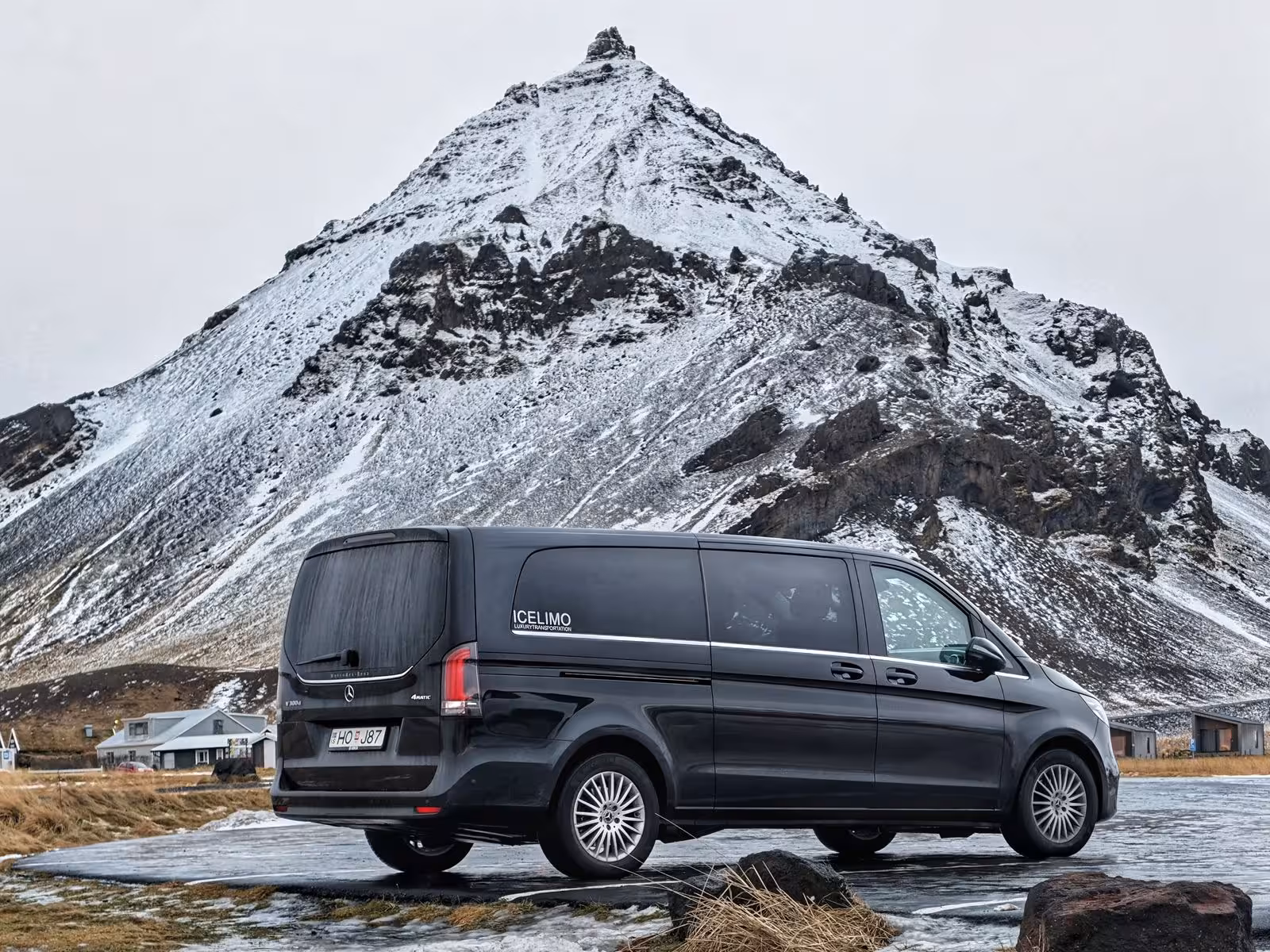 Black Mercedes V-Class van by Icelimo parked in front of a snow-capped mountain peak in Iceland
